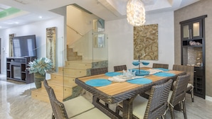 A modern dining area with a glass staircase, wicker furniture, and a chandelier.