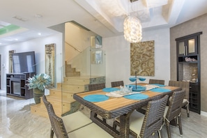 Un espace de repas moderne avec un escalier en verre, des meubles en osier et un lustre.