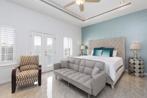 Une chambre à coucher comprenant un lit, deux tables de chevet, un ventilateur de plafond et un canapé.