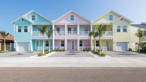A row of three-story houses with balconies, a driveway, and small palm trees. - Luxury Coastal Retreat​​​​​​​ • Heated Pool & Hot Tub • 3 Min Walk to Beach (South Padre Island)