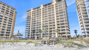 A beachfront hotel with multiple floors, balconies, and a sandy beach area with a small structure. - Totally Beachin - Condo with Stunning Ocean Views (Orange Beach)
