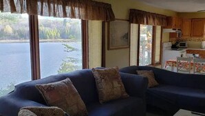 Ein Wohnzimmer mit einem dunkelblauen Sofa, gemusterten Kissen und Blick auf einen See durch große Fenster.