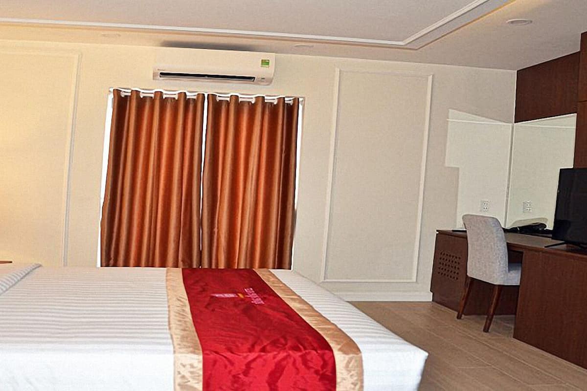 A hotel room with a bed, a desk, a television, and an air conditioning unit.