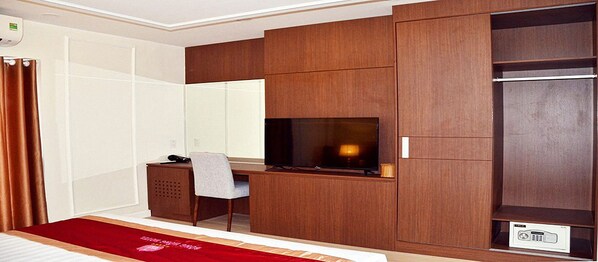 A hotel room with a bed, a desk with a chair, a television, and a wardrobe.