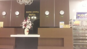 A reception desk with a sign for BONG HONG HOTEL, a clock, and a vase of flowers. - Bong Hong Hotel (Sa Dec)