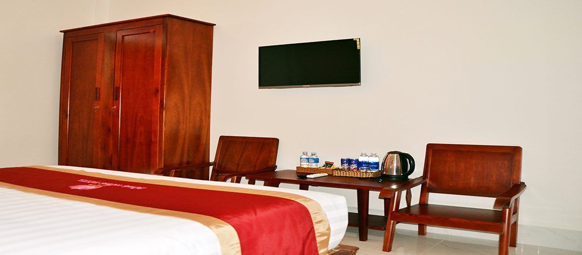 Ein Hotelzimmer mit einem Bett, zwei Holzstühlen, einem kleinen Tisch mit Wasserflaschen und einem Wasserkocher sowie einem Kleiderschrank.