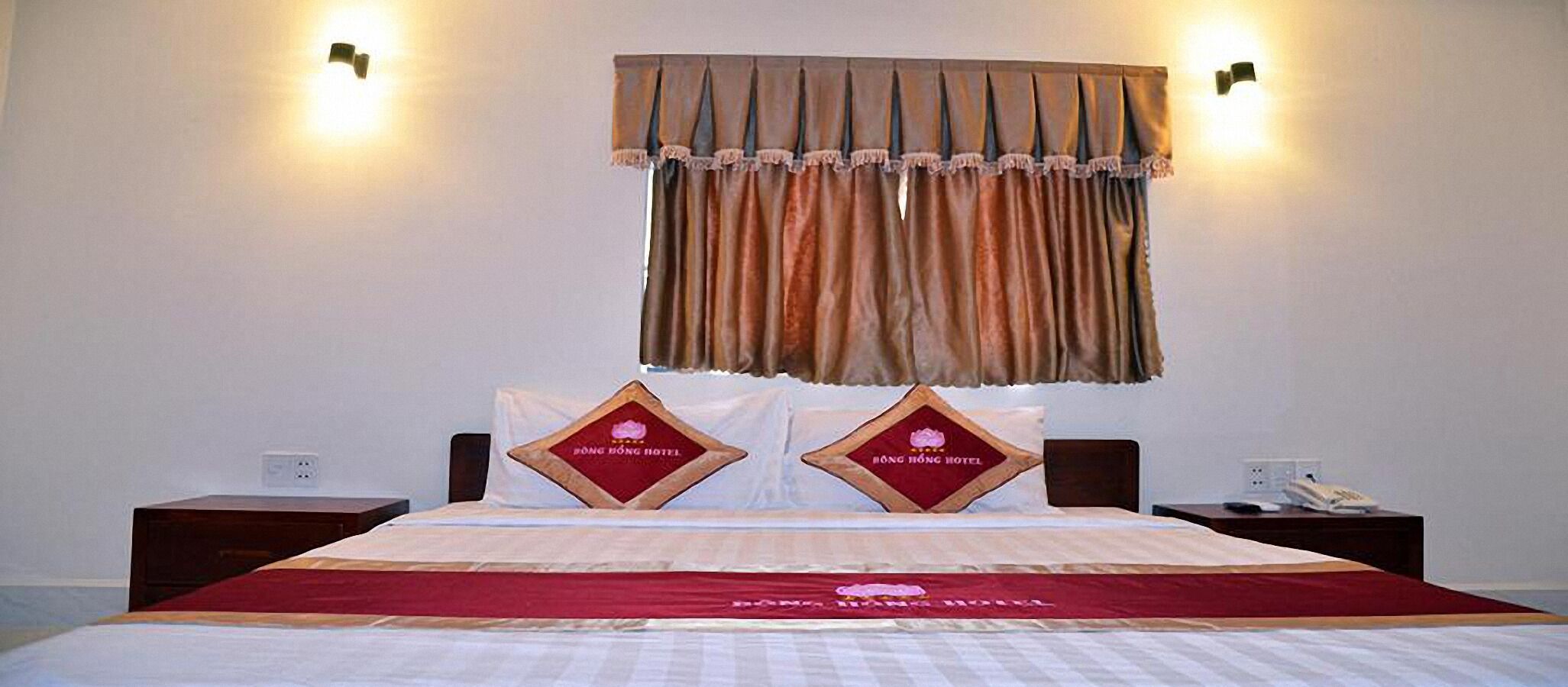 A hotel room with a large bed, two nightstands, a red bedspread, and a decorative headboard.