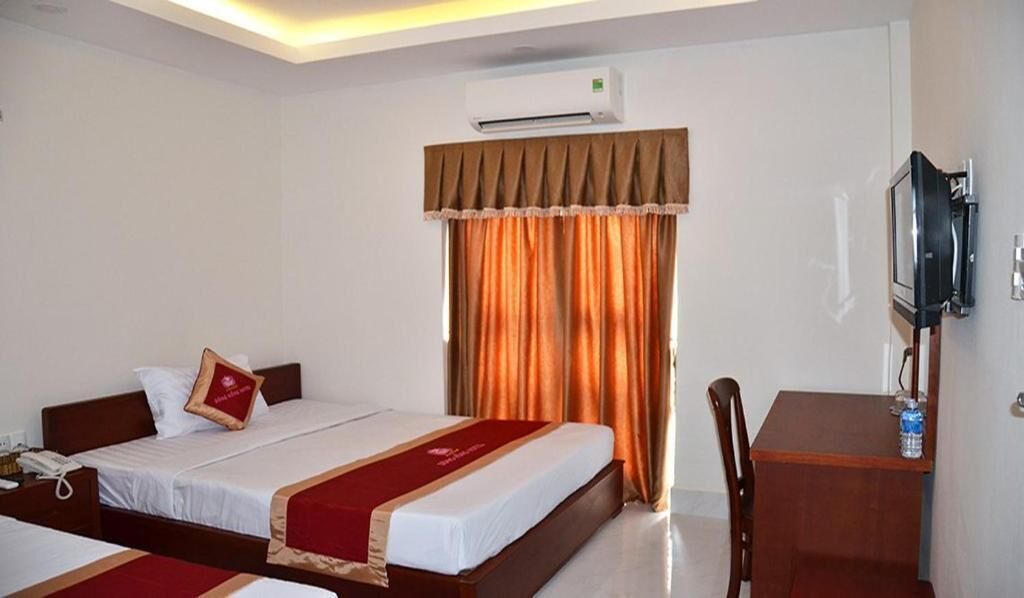 A hotel room with two beds, a desk, a television, and an air conditioning unit.