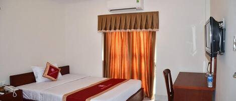 A hotel room with two beds, a desk, a television, and an air conditioning unit.