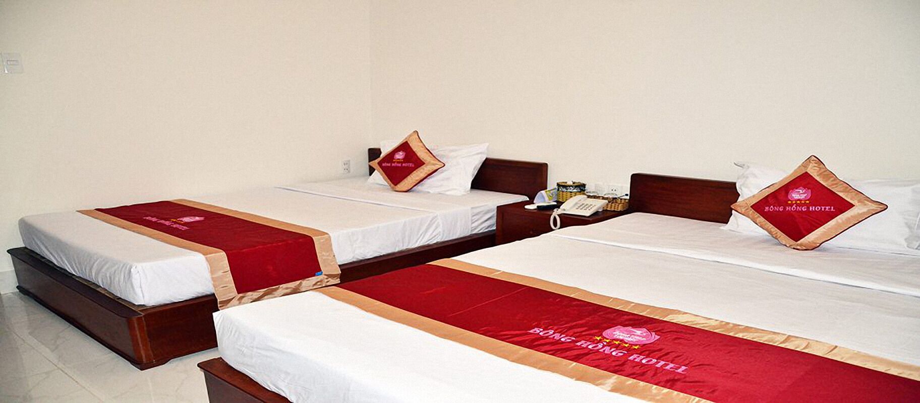 Een hotelkamer met drie eenpersoonsbedden, elk voorzien van een rode bedloper en een kussen met het logo van het hotel.