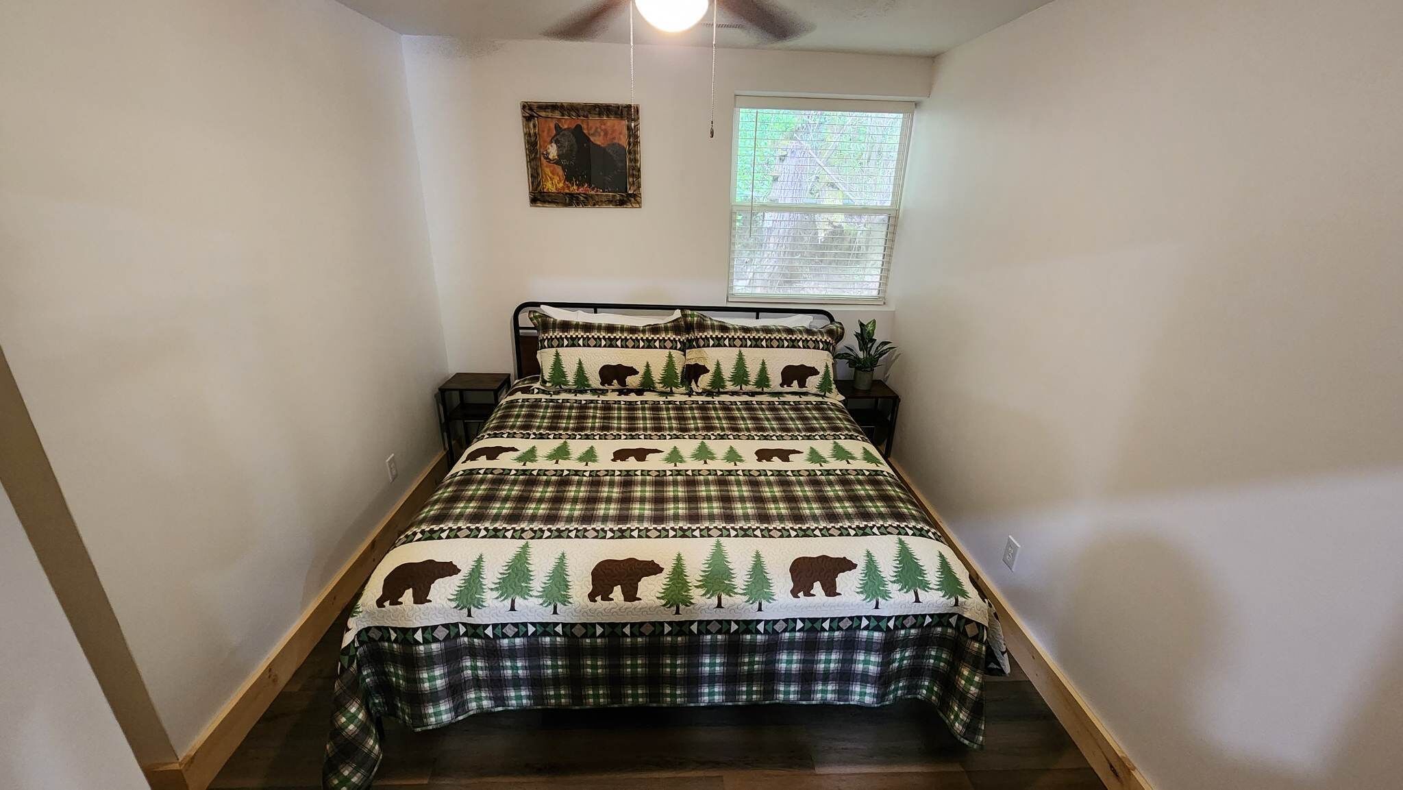 Ein Schlafzimmer mit einem Bett, einem Fenster mit Jalousien, einem Deckenventilator und einem kleinen Tisch mit einer Pflanze.