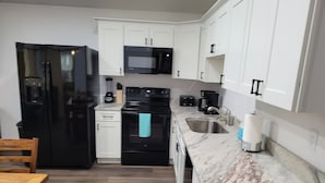 A compact kitchen with white cabinets, a black refrigerator, a microwave, a stove, and a sink. - Jason's Log Cabin Retreat w/ Hot tub, rockers, swing, game room, & 3 King beds (Sevierville)