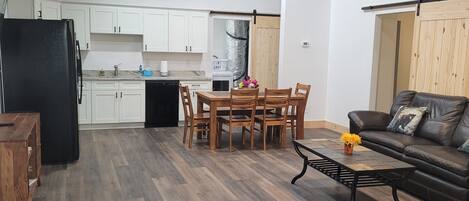 Une cuisine moderne avec des meubles blancs, un réfrigérateur noir et un coin repas comprenant des chaises et une table en bois.