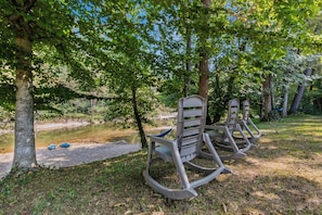 A serene outdoor seating area with rocking chairs and a small pond. - Ronnies Riverfront Porch Swing w/ Hot Tub, Arcade, Kayaks, Riverfront, & 4 Kings (Sevierville)