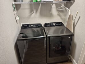 A laundry room with two black front-loading washers and dryers, a white wall, and a hanging rack.