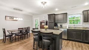 A modern kitchen with dark wood cabinets, a central island with bar stools, a built-in dishwasher, and a window with a view of greenery.