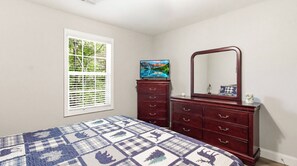 Ein Schlafzimmer mit Bett, Kommode, Spiegel und Fenster mit Jalousien.