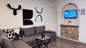 A modern living room with a grey sofa, a coffee table, and abstract wall art. A television is mounted on the wall, and a no-smoking sign is visible. - Private House with 8 Bedrooms: Sleeps 16 | Across from Jalisco Stadium. (Independencia)