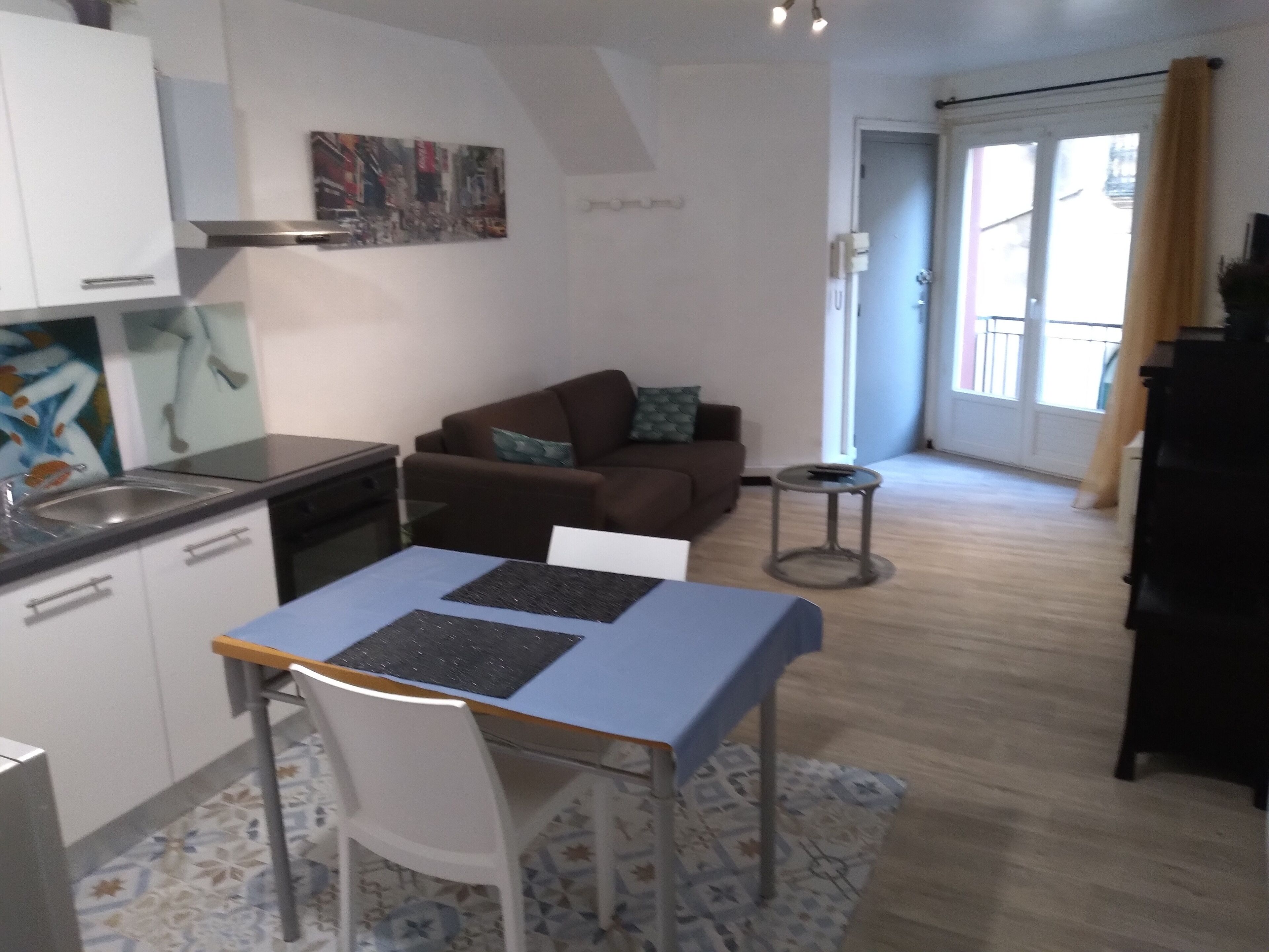 Un espace de vie compact comprenant un coin cuisine, un coin repas avec une table et des chaises, un canapé avec un coussin et une petite table d’appoint.
