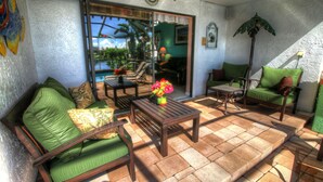Eine Terrasse mit einem Holztisch, zwei grünen Sitzgelegenheiten mit Polstern und einer Couch mit gemusterten Kissen.