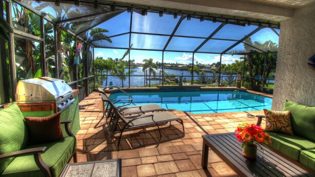 Ein überdachter Außenbereich mit Pool, grünen Möbeln und Grill.