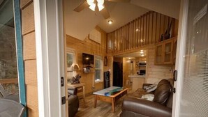 A cozy cabin interior with a wooden dining table, a leather sofa, and a kitchen area with wooden cabinets.