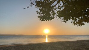 A beach with a sunset over the water, sandy shore, and a tree in the foreground. - Sinclair Bay Resort (Unit 1) - Peaceful waterfront retreat on private estate (PROSERPINE)