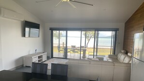 A modern kitchen with a dining area, large windows overlooking a beach, and a ceiling fan. - Sinclair Bay Resort (Unit 1) - Peaceful waterfront retreat on private estate (PROSERPINE)