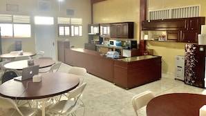 Uma cozinha compacta com ilha central, área de jantar com cadeiras e uma geladeira.