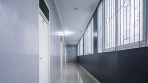 Um corredor comprido e estreito com uma porta branca à esquerda e grandes janelas à direita.