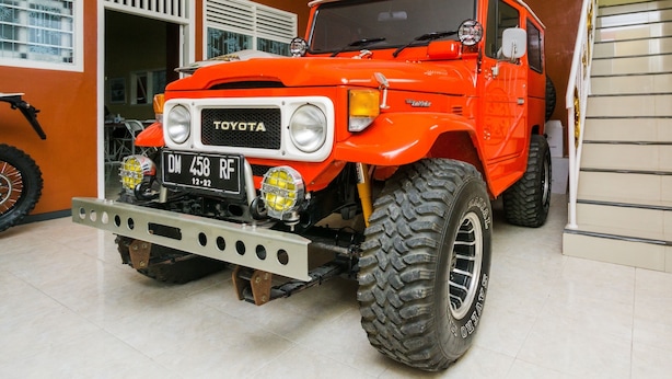 Um Toyota Land Cruiser vermelho numa garagem com soalho em azulejos e uma janela com persianas.
