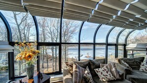 Et hyggeligt rum med et stort vindue, en sofa med mønstrede puder og en vase med blomster på et træbord.