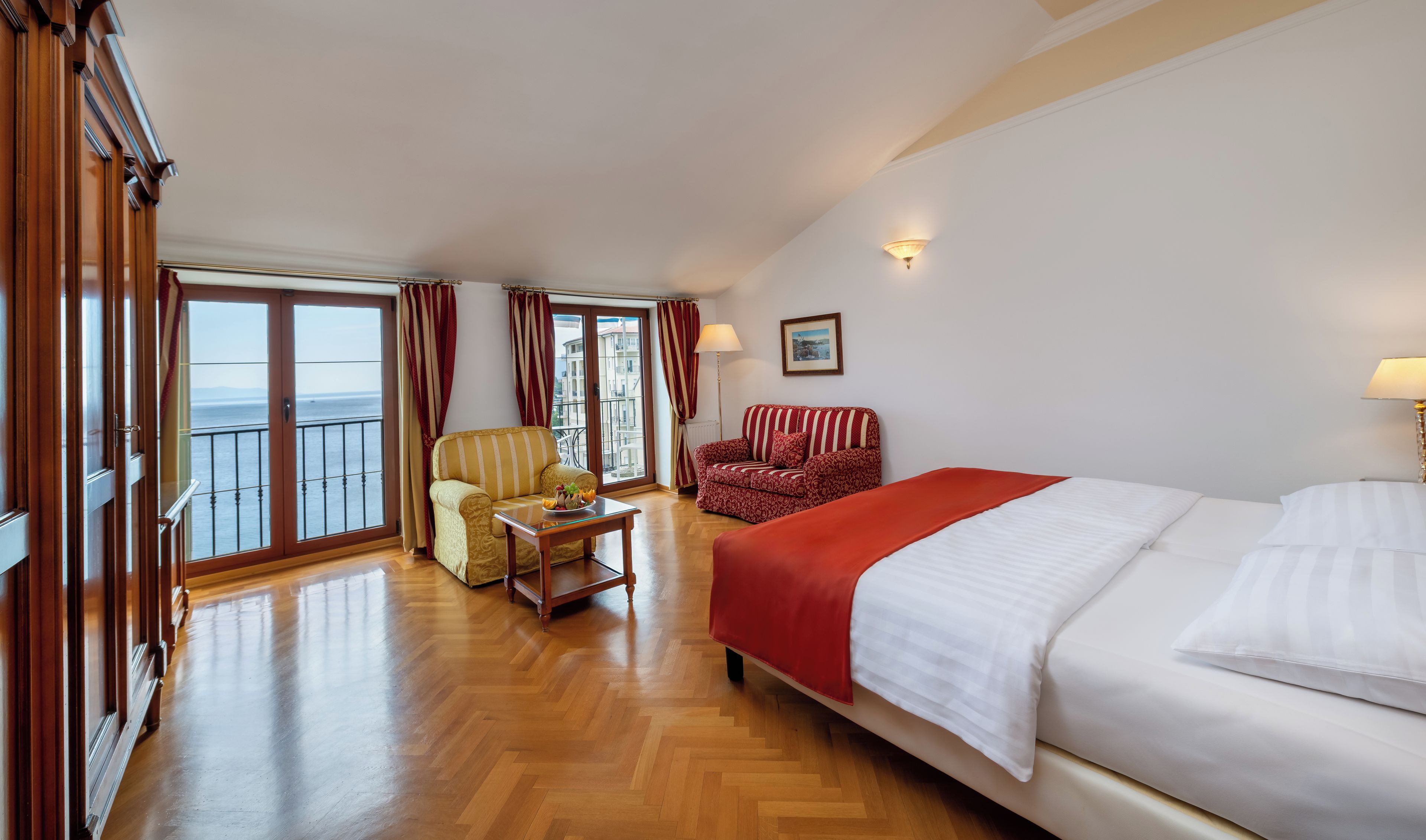 Ett hotellrum med en säng, en soffa, en stol, ett bord och utsikt över havet från en balkong.