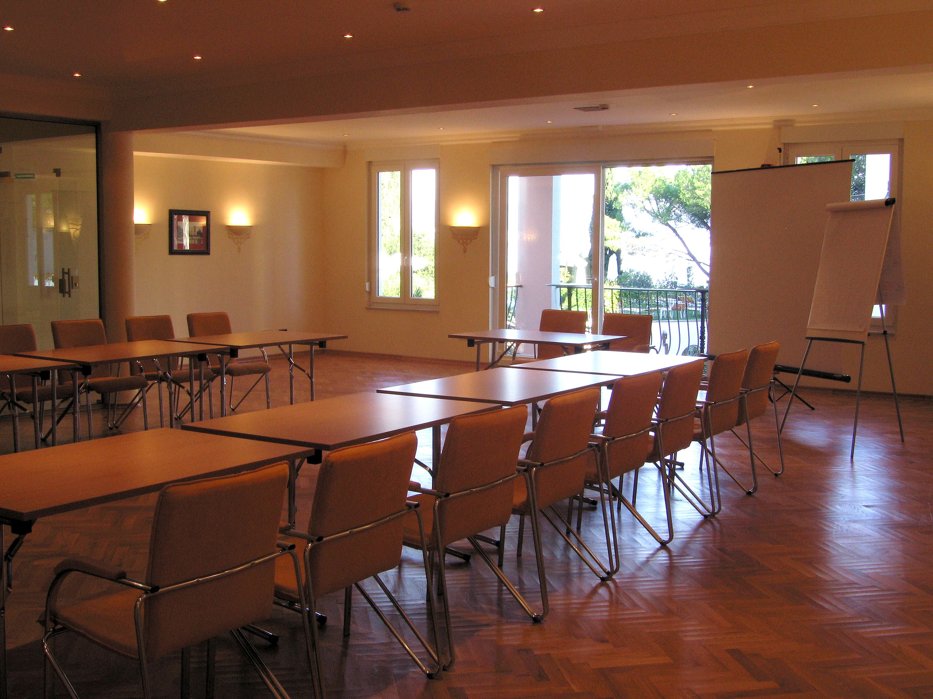 Ein Konferenzraum mit Tischen, Stühlen, einer Whiteboard-Tafel und Blick ins Freie durch große Fenster.