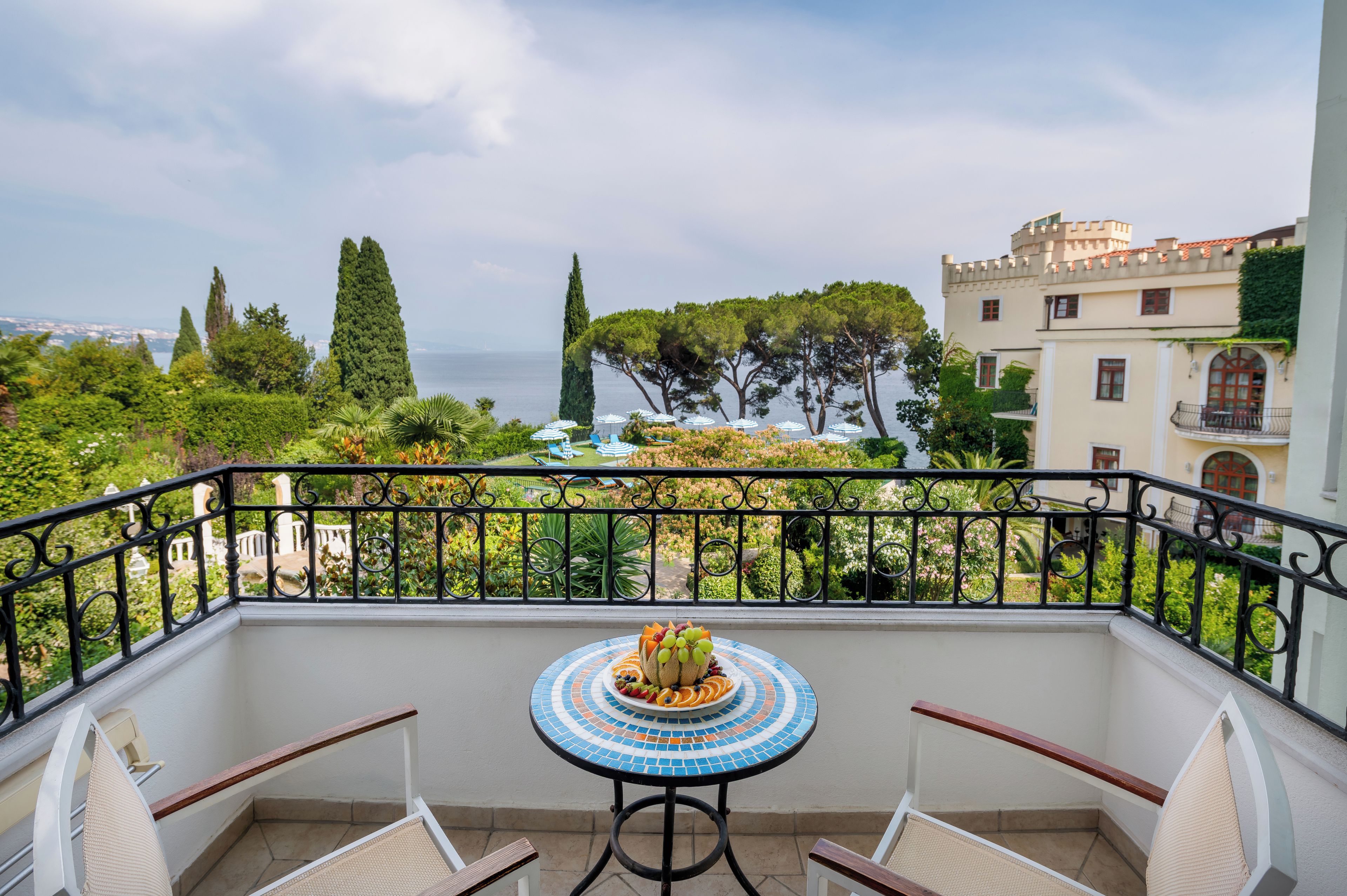 Un balcon avec une table dressée pour le dîner, donnant sur un jardin et offrant une vue sur la mer.