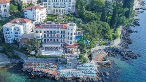 Luftaufnahme eines Küstenhotels mit mehreren Gebäuden, einer felsigen Küstenlinie und einem Poolbereich mit Liegestühlen.