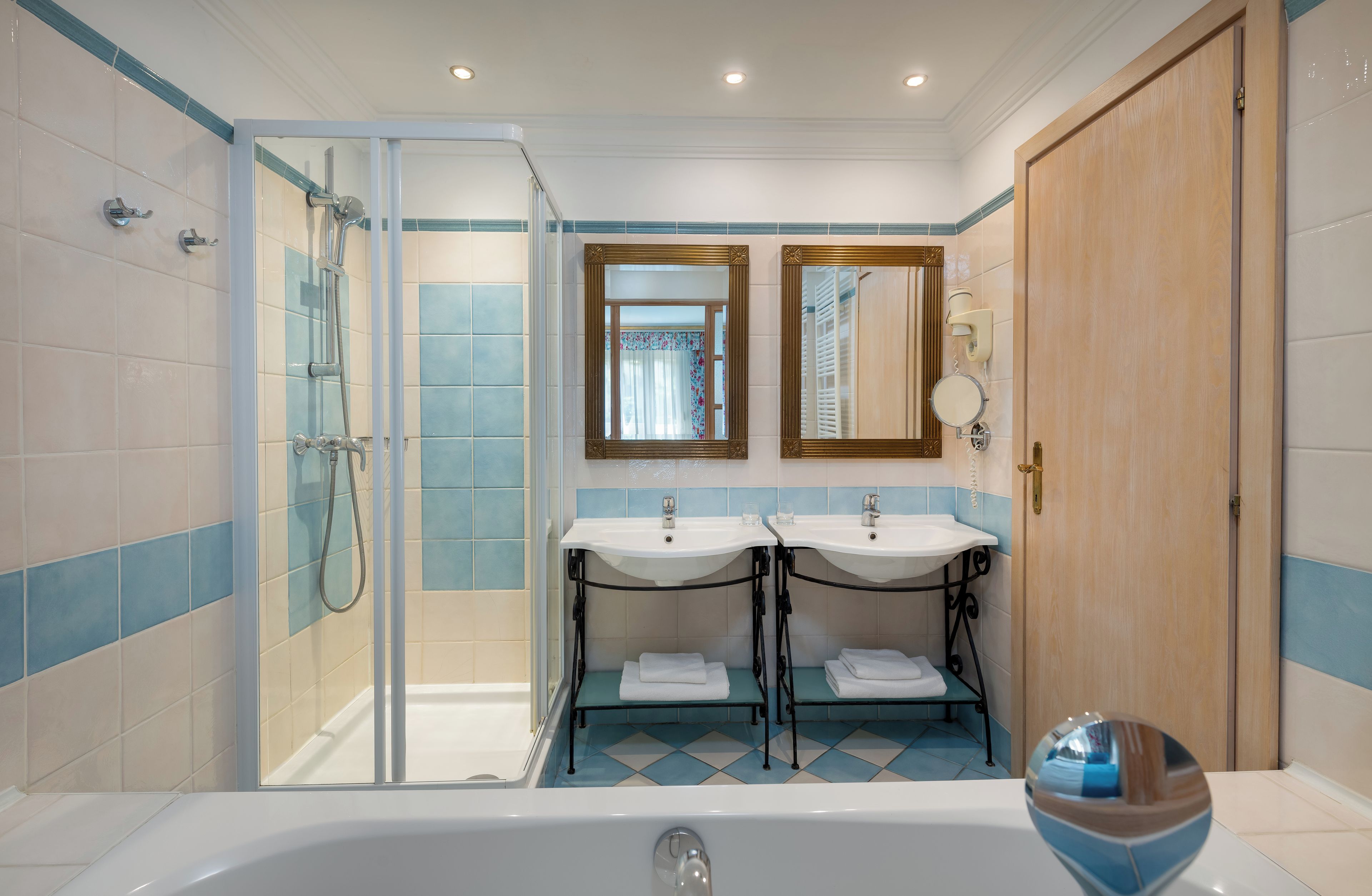 A bathroom with a glass-enclosed shower, two sinks with mirrors above, and a wooden door.