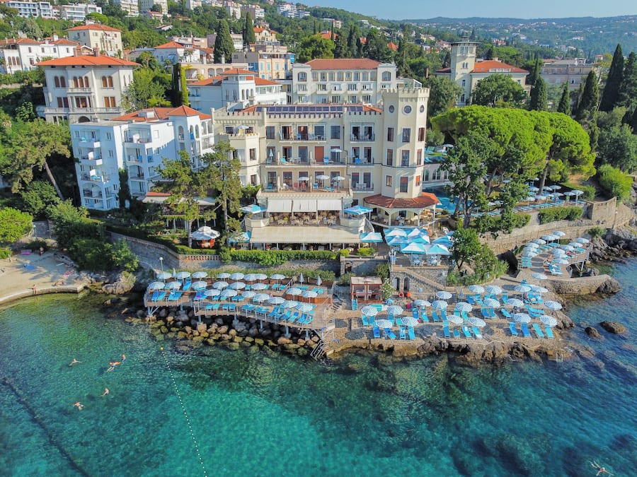 A coastal hotel with multiple balconies, a pool area, and a view of the sea.
