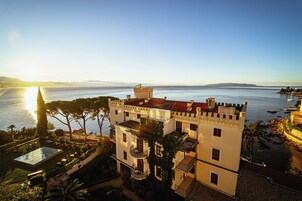 Un edificio parecido a un castillo con piscina, rodeado de vegetación y vistas a un cuerpo de agua.