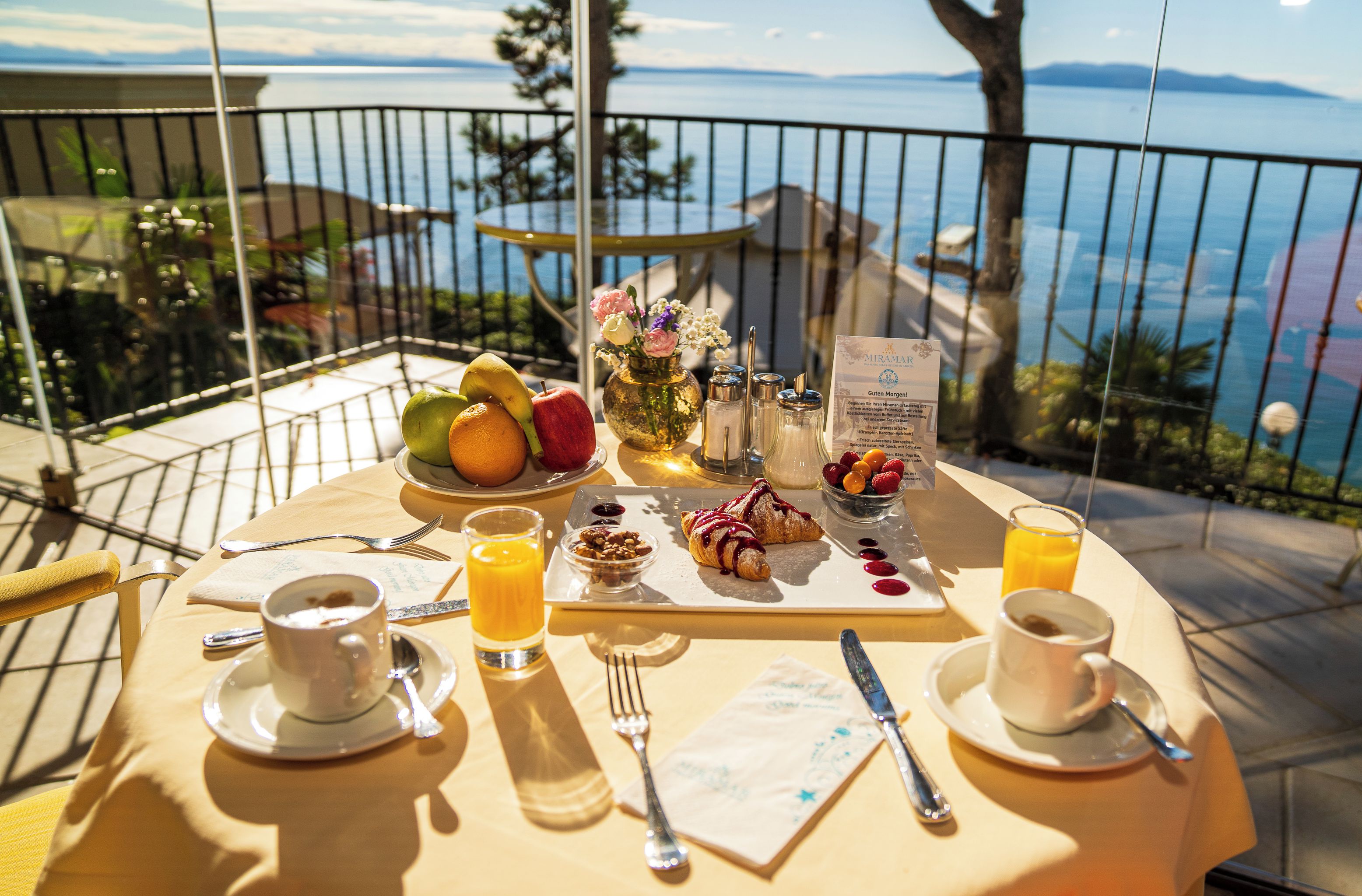 Une table de petit-déjeuner dressée avec des fruits, des viennoiseries et des boissons, offrant une vue panoramique.