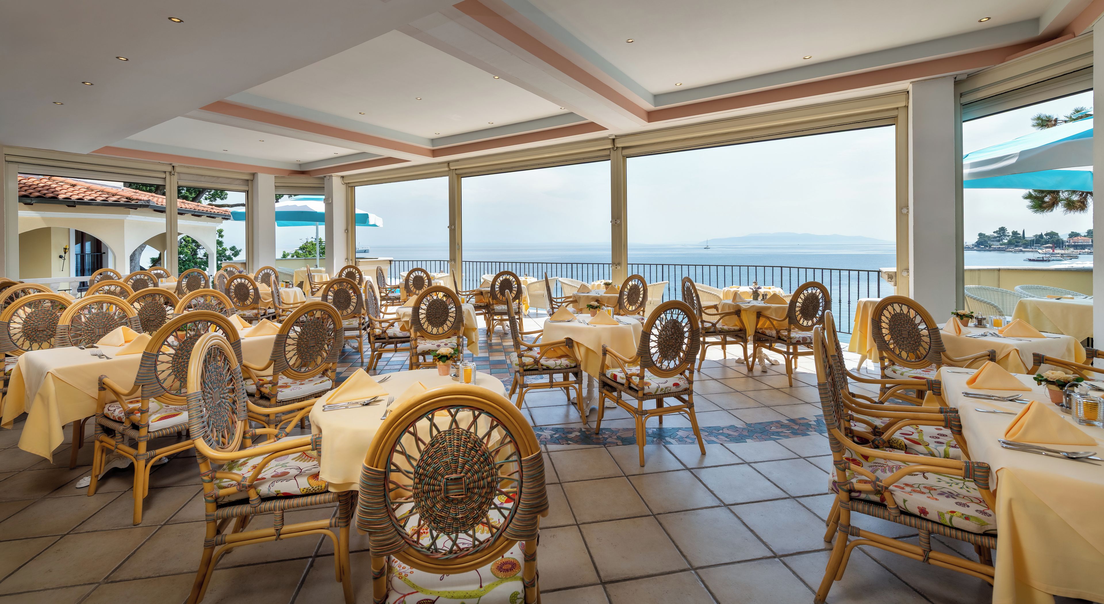 Een restaurant met terras, rieten stoelen en tafels met gele tafelkleedjes.