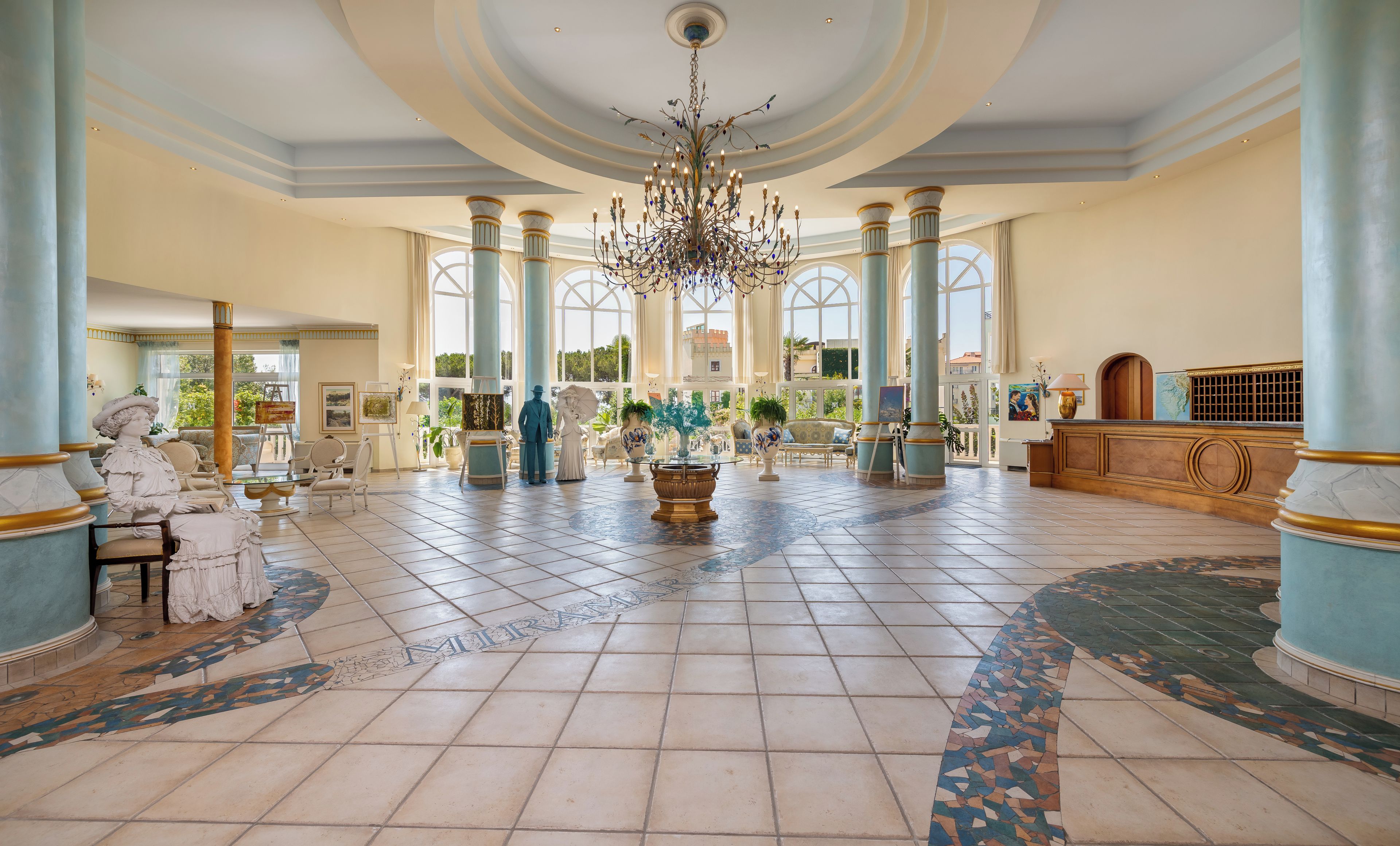 Eine geräumige Lobby mit einem prächtigen Kronleuchter, Säulen und einem Fliesenboden mit Mosaikbordüre.