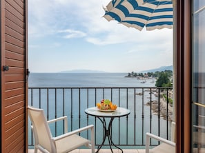 Ein Balkon mit Tisch und Stühlen, der auf ein Gewässer mit Booten und eine ferne Küste blickt.