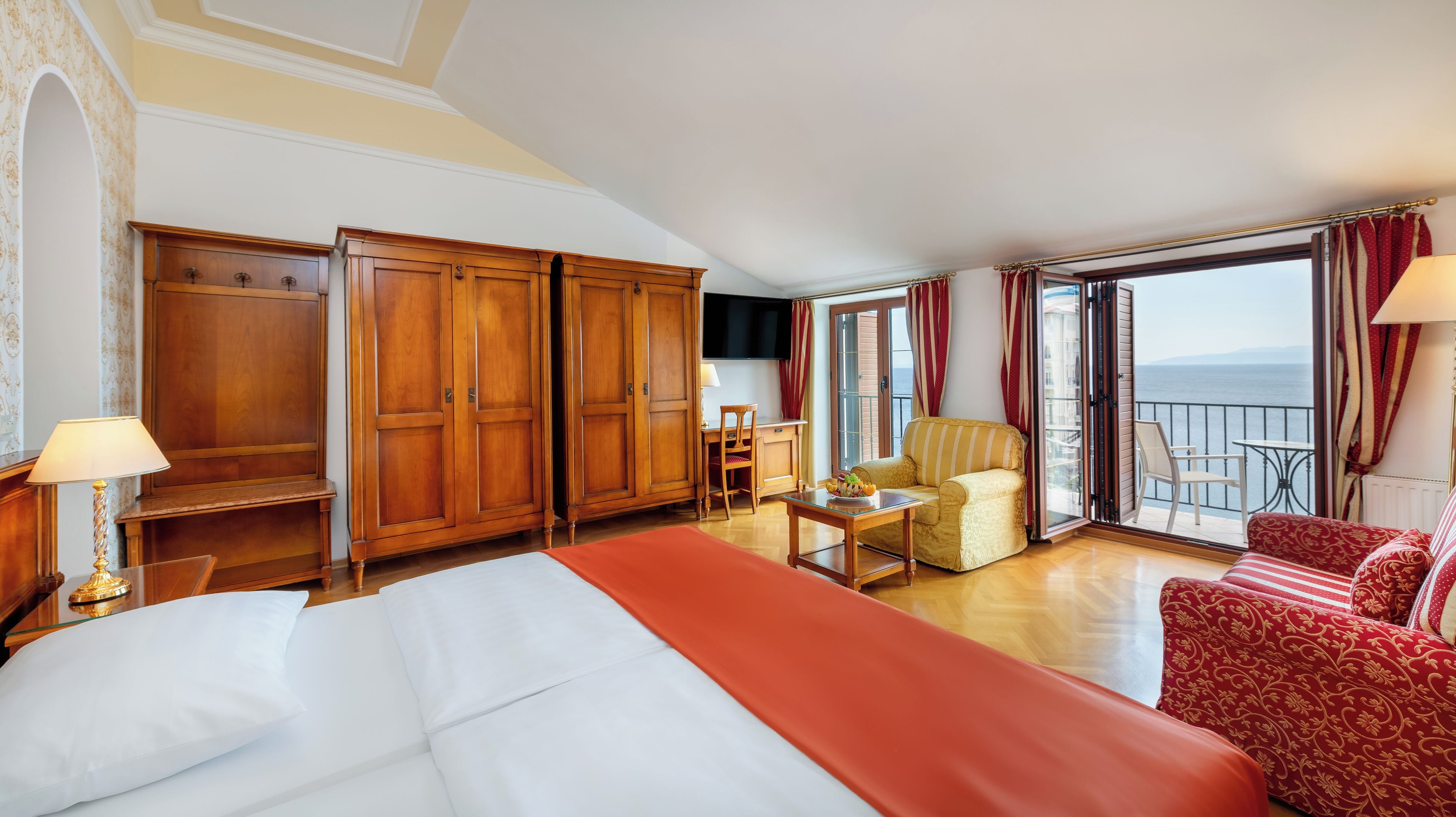 A hotel room with a bed, a desk, a chair, a sofa, and a balcony with a view.