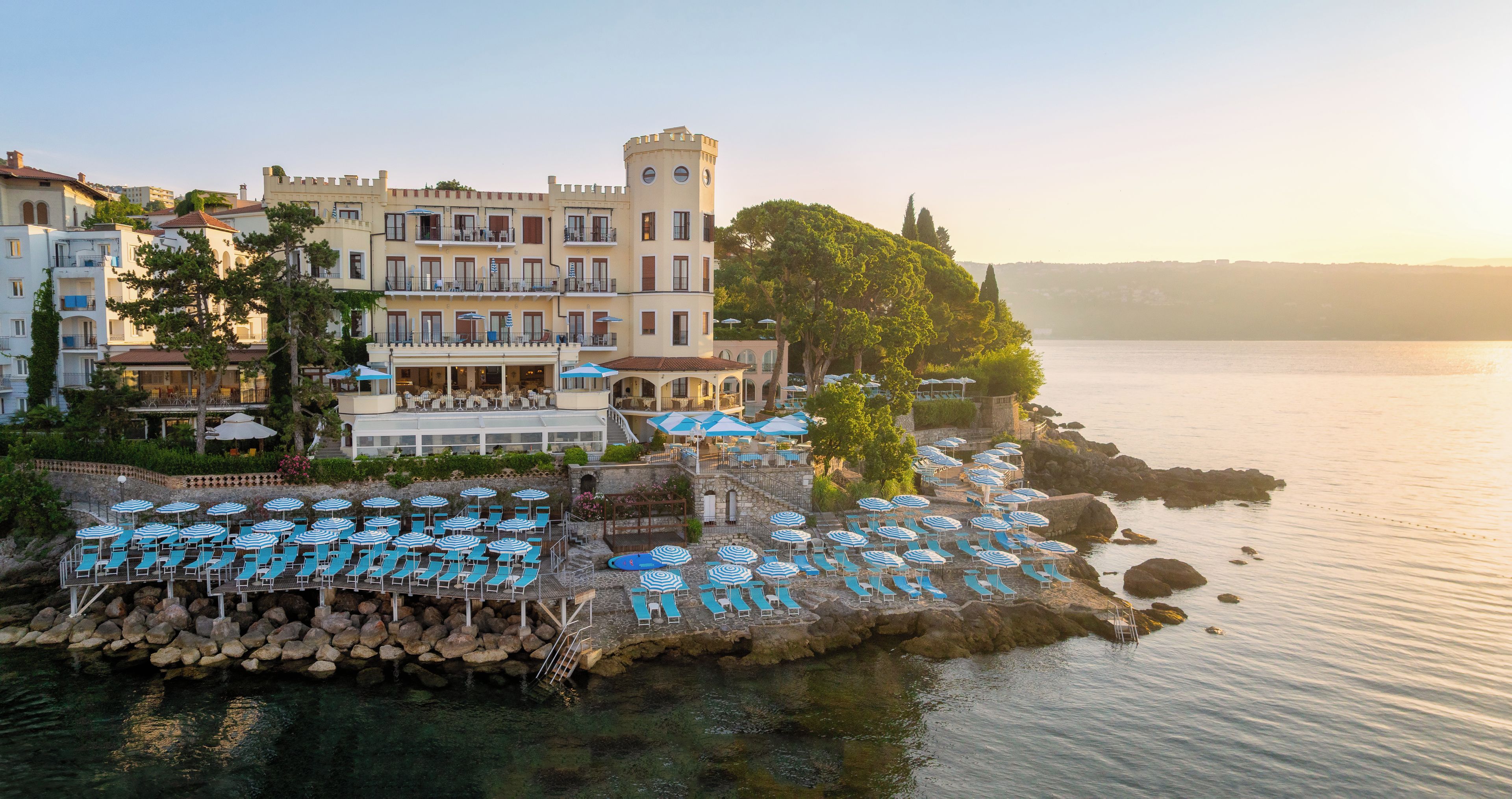 A coastal hotel with a pool area, outdoor seating, and a view of the sea.