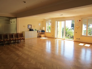 Ein geräumiges Zimmer mit Fischgrätparkett, einer Küchenzeile, einem Essbereich mit Stühlen und großen Fenstern mit Blick auf Grünflächen.