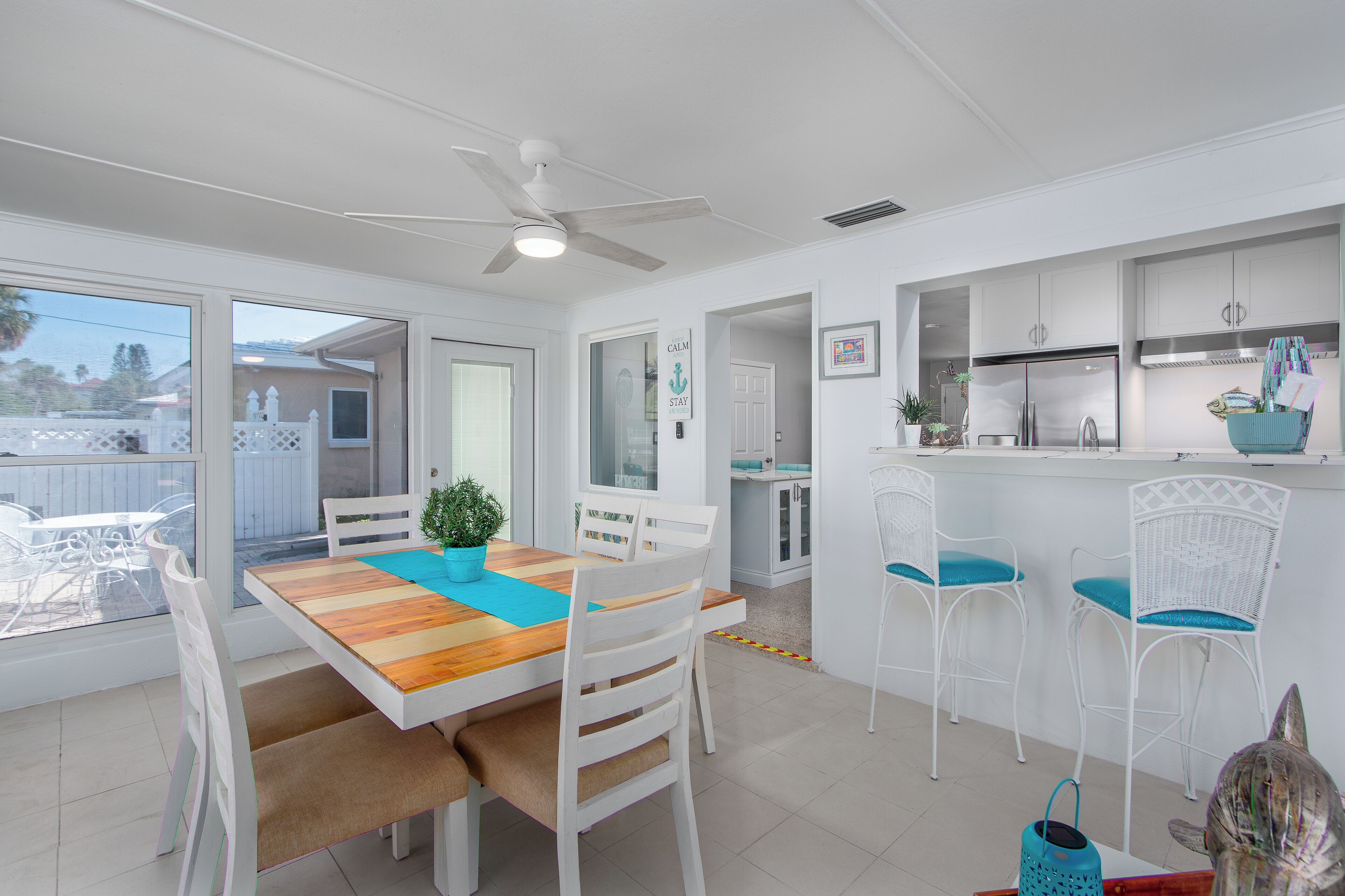A bright kitchen with white cabinets, a stainless steel refrigerator, and a dining area with a wooden table and white chairs.