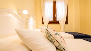 Un lit avec des oreillers blancs ornés de motifs floraux, une table de chevet avec une lampe et une fenêtre avec des rideaux.