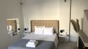 A neatly made bed with white linens, two bedside tables with lamps, a mirror on the wall, and a vase with dried plants. - Greece Apartments Now (Patra Achaia)