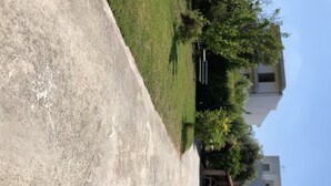 A paved pathway adjacent to a grassy area with a building in the background. - Greece Apartments Now (Patra Achaia)